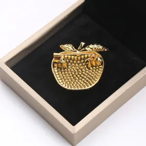 Detailed macro view of the back of a golden apple brooch showing the pin safety catch.