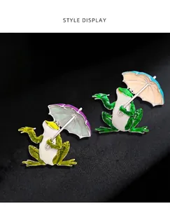 Detailed close-up showing two whimsical frog brooches holding colorful dripping oil umbrellas.