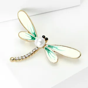 Close-up of elegant gold dragonfly brooch with pearl, crystals and green enamel wings