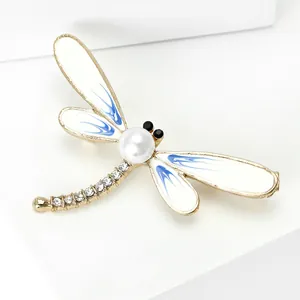 Detail view of gold dragonfly brooch with white pearl center and blue enamel wings