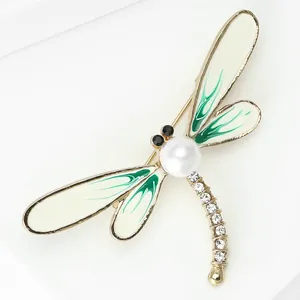 Detailed view of an elegant dragonfly brooch with green enamel, pearl, and crystals