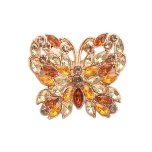Élégante broche papillon avec des strass orange et jaunes étincelants sur fond blanc.