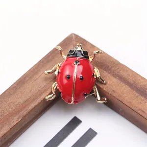 Gros plan d'une broche coccinelle créative rouge avec pattes dorées et points noirs émaillés.