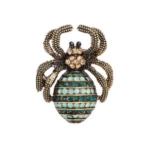 Gedetailleerde macro-opname van een vintage spinnenbroche met groene en blauwe kristallen.