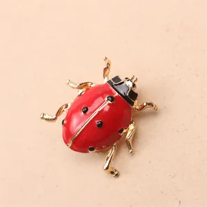 Gros plan détaillé d'une broche coccinelle en émail rouge et or sur un fond neutre