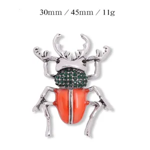 Detailweergave van keverbroche met groene strass-steentjes en oranje emaille
