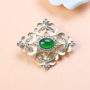Detailed close-up of vintage Baroque style gold brooch with green stone and crystals
