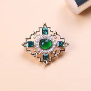 Macro view of detailed vintage Baroque brooch with green gemstone and white pearl accents