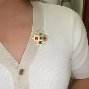 Close-up of a vintage baroque matte gold brooch with colorful gemstones on a cardigan