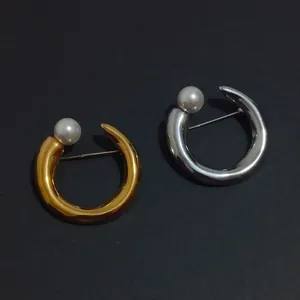 Detailed view of elegant C-shaped metallic brooches with pearls in gold and silver