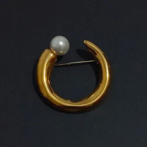 Detailed macro view of an elegant C-shaped gold metal brooch with a white pearl inlay