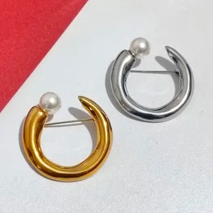Detail of gold and silver C-shaped metallic brooches with pearls for elegant suits.