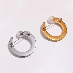 Detailed view of elegant C-shaped metal brooches featuring pearls in silver and gold