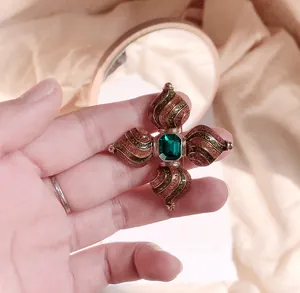 Detail van een vintage barokke kruisbroche met smaragdsteen en goud emaille krullen