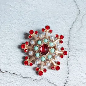 Macro view of a luxury Baroque snowflake brooch featuring red crystals and white pearls
