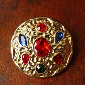 Close-up of vintage gold hammered brooch with colorful inset gemstones in royal style.