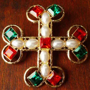 Close-up of vintage palace style cross brooch with red green crystals and pearls.