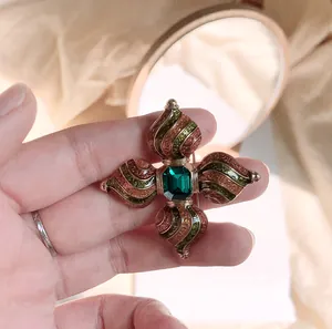 Gedetailleerde close-up van een vintage barokke kruisbroche met een groene steen