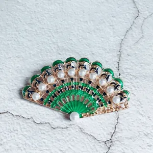 Close-up of a vintage luxury green enamel fan-shaped brooch with white pearls.