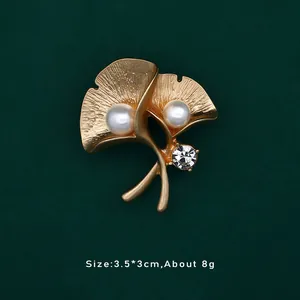 Dettaglio macro di spilla foglia ginkgo dorata vintage con perle e strass