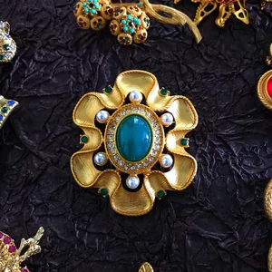 Detailed view of luxury baroque vintage brooch with green gemstone and pearls.