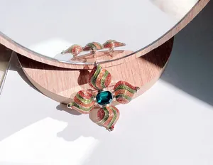 Gedetailleerd overzicht van een vintage barokke emaille kruisspeld met groene edelsteen