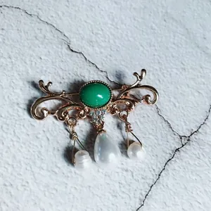 Close-up detail of a vintage baroque brooch featuring a green center and pearl pendants.