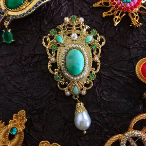 Close-up of luxury retro gold brooch with green gemstone and teardrop pearl drop