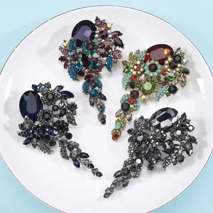 Four vintage rhinestone brooches in various colors displayed on a white plate