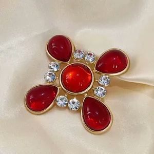 Nahaufnahme einer roten Vintage-Kreuzbrosche mit goldfarbenem Metall und Kristallen