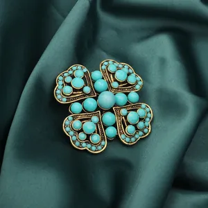 Vintage heart-shaped brooch with turquoise blue beads displayed on dark green silk fabric