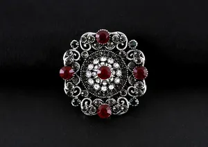 Detalle de broche barroco vintage con diseño calado intrincado y cristales rojos.