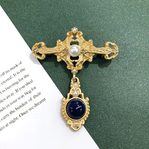 Detail van een vintage broche in barokstijl in mat goud met parels en een blauwe edelsteen.