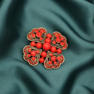 Close-up macro of a vintage heart-shaped brooch with red beads on dark green silk.