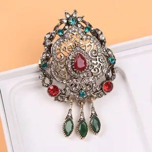 Détail d'une broche de cour vintage luxueuse avec des gemmes colorées et des pendentifs larmes.