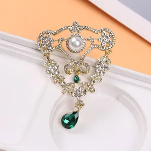 Vue rapprochée détaillée d'une broche de style cour vintage avec cristaux émeraude et perle.