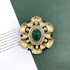 Detailweergave van een vintage barokke broche met een groene steen en een matgouden afwerking