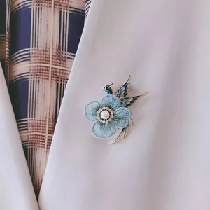 Detailed macro view of a vintage handmade embroidered bird and flower brooch with pearl