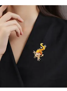 Detailansicht einer goldenen Drachenbrosche mit orangefarbenem Emaille auf einem Blazer.