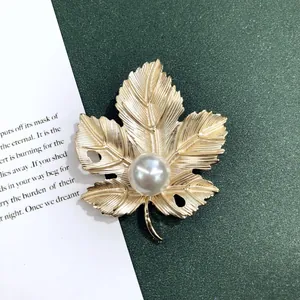 Detailopname van vintage matgouden esdoornblad broche met grote parel midden
