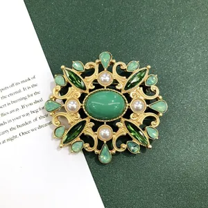 Gedetailleerde weergave van een vintage barokke broche in mat goud met groene stenen.