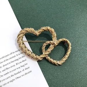 Gedetailleerde macro-opname van een vintage matgouden broche met twee harten en touwtextuur.