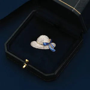 Nahaufnahme einer eleganten Hut-Brosche mit funkelnden Kristallen und blauer Emaille-Schleife