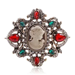 Broche camafeo vintage de estilo palacio con cristales rojos y verdes sobre blanco.