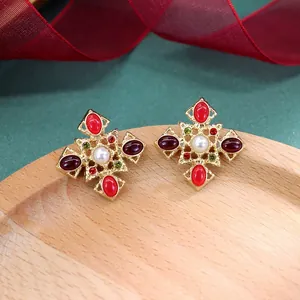 Detail van barokke vintage kruisoorbellen met rode strass-steentjes en centrale parel.