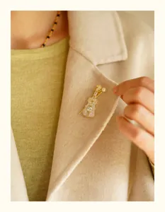 Close-up of an elegant violin-shaped gold brooch with crystals on a beige coat lapel.