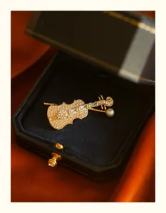 Detailed close-up of a gold violin brooch with crystals and a pearl in a premium jewelry box