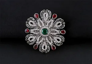 Détail d'une broche baroque avec cristaux verts et rouges sur fond texturé noir
