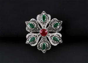 Détail de la broche vintage baroque avec cristaux verts et rouges sur fond noir
