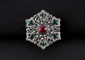 Gros plan d'une broche vintage baroque avec cristaux rouges et verts et filigrane fin